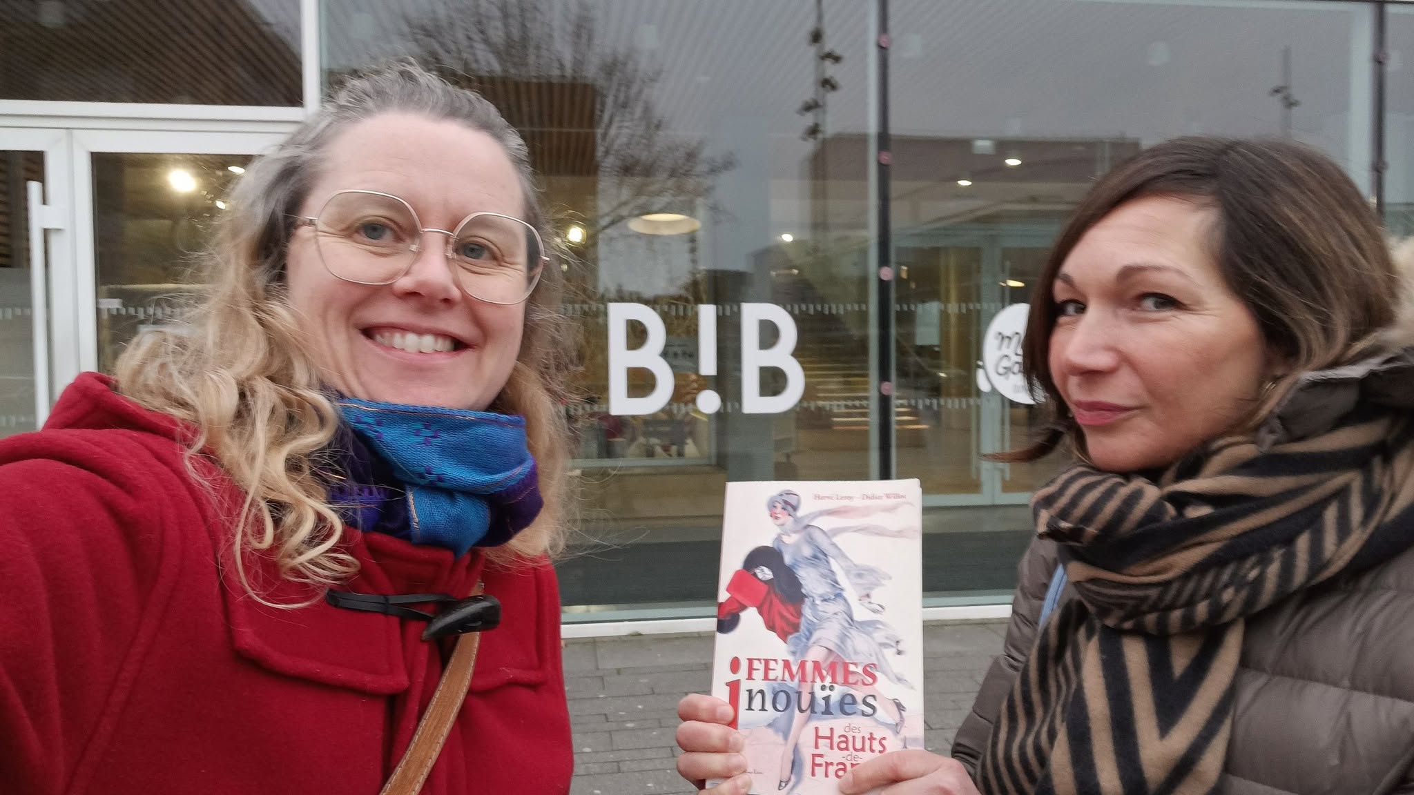 Deux membres de la troupe tenant l'ouvrage Femmes inouïes devant la Bibliothèque de Dunkerque